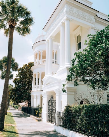 White antebellum mansion with tall columns and palm trees on a sunny day