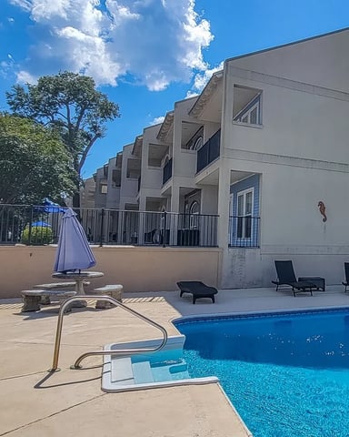 Outdoor pool with lounge chairs beside the property under a bright blue Gulf Coast sky