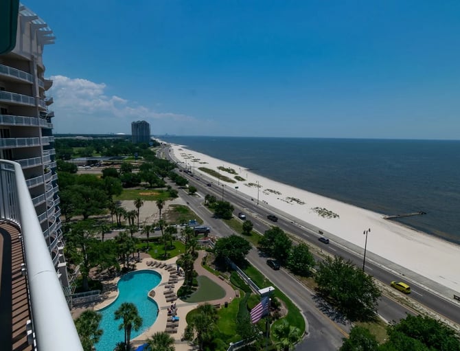 Beachfront High-Rise Resort With Pool, Landscaped Grounds, Sandy Beach, And Ocean View Under Clear Blue Sky
